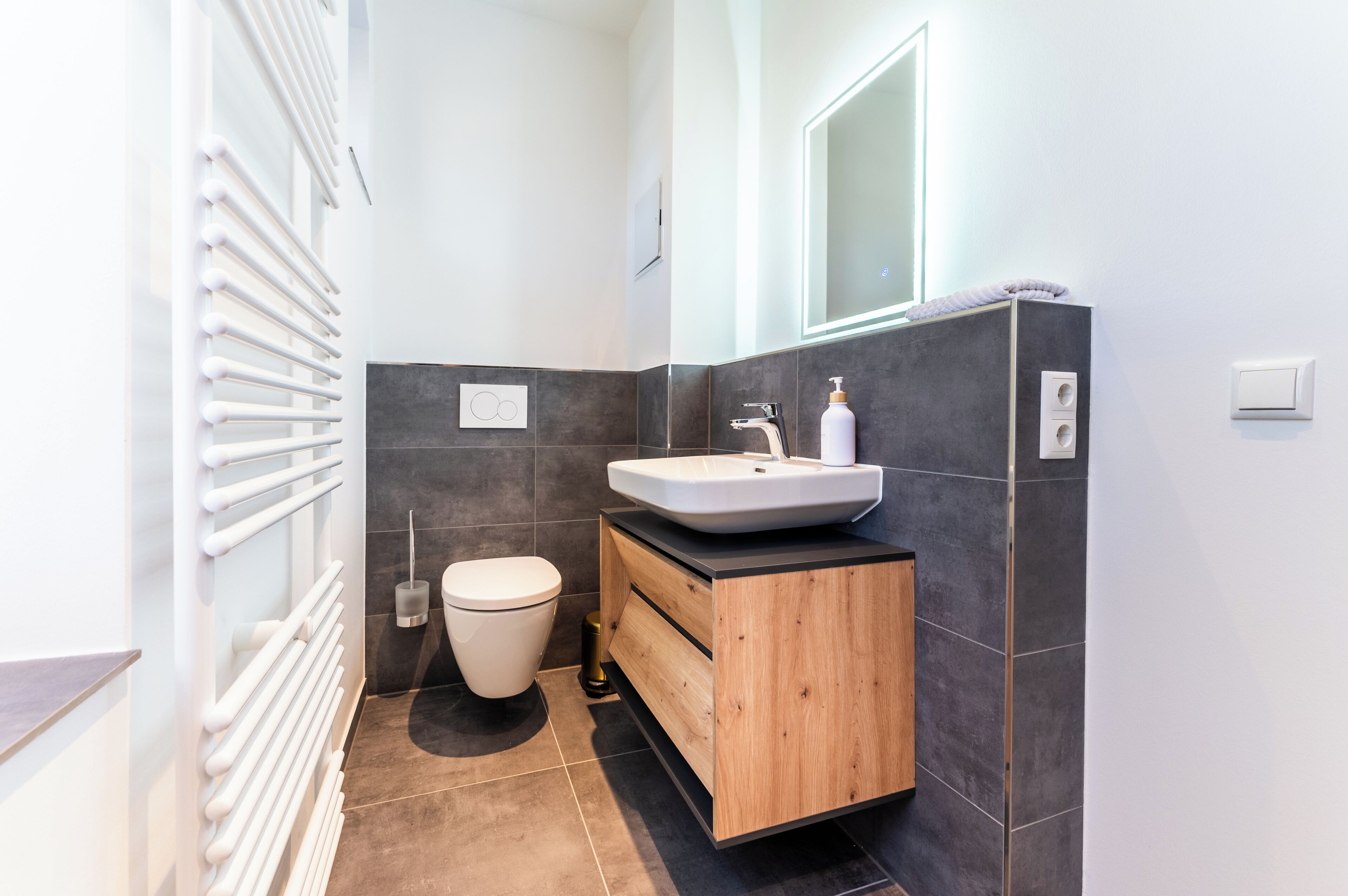 A modern bathroom with a white sink, wooden vanity, and a toilet.
