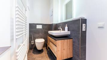 A modern bathroom with a white sink, wooden vanity, and a toilet.