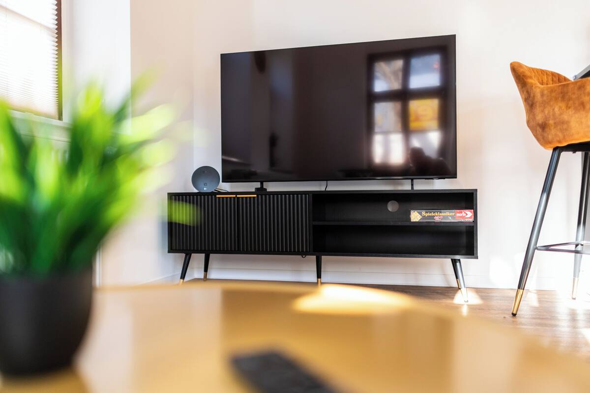 A modern living room with a flat-screen TV on a black stand, a potted plant, and a brown chair.