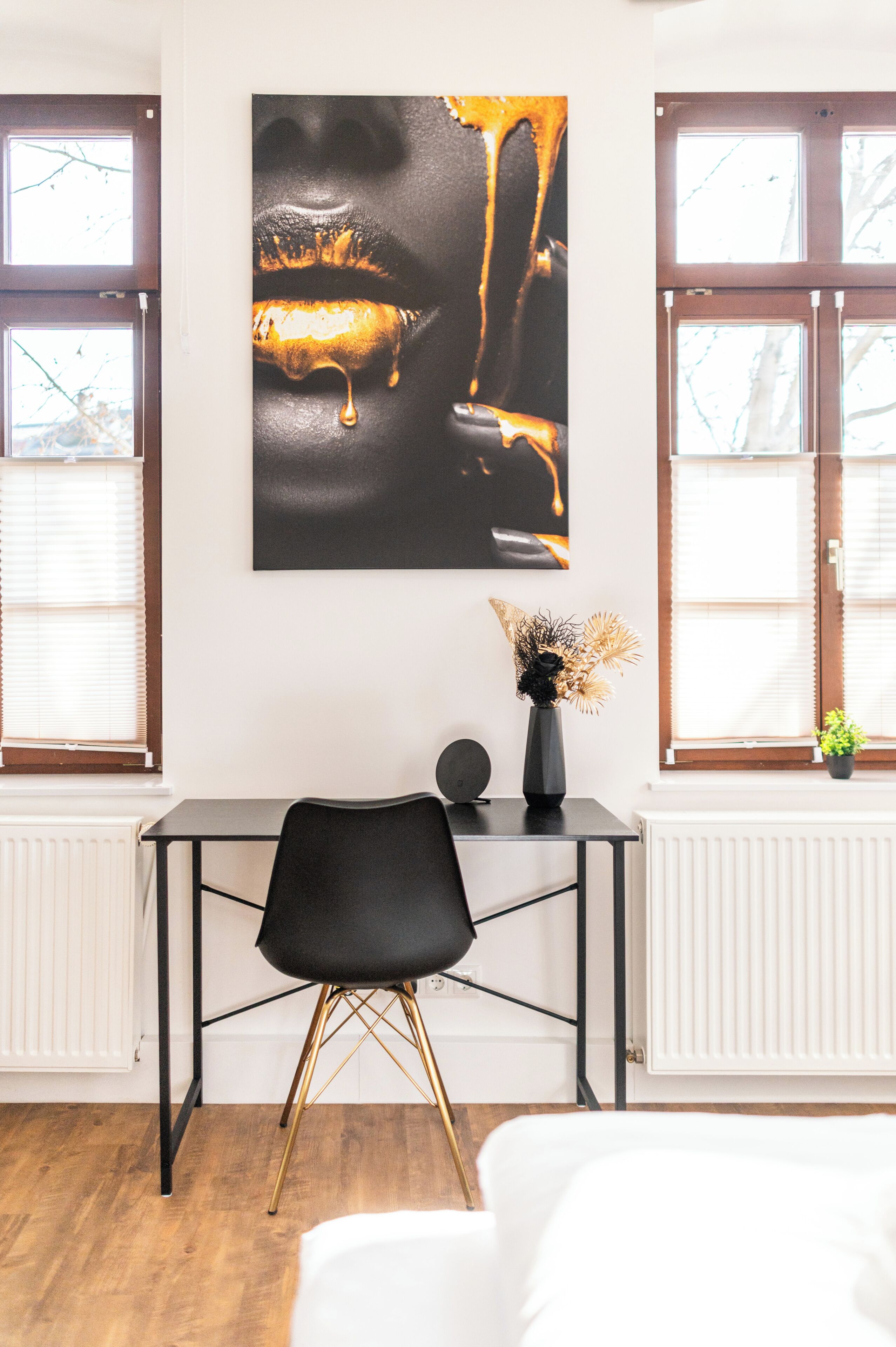 A modern room with a black desk, a black chair, a large abstract painting, and a window with blinds.