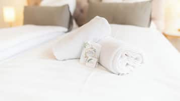 Een keurig opgemaakt bed met witte lakens, een opgerolde handdoek en een klein kaartje met een bloemendecor.