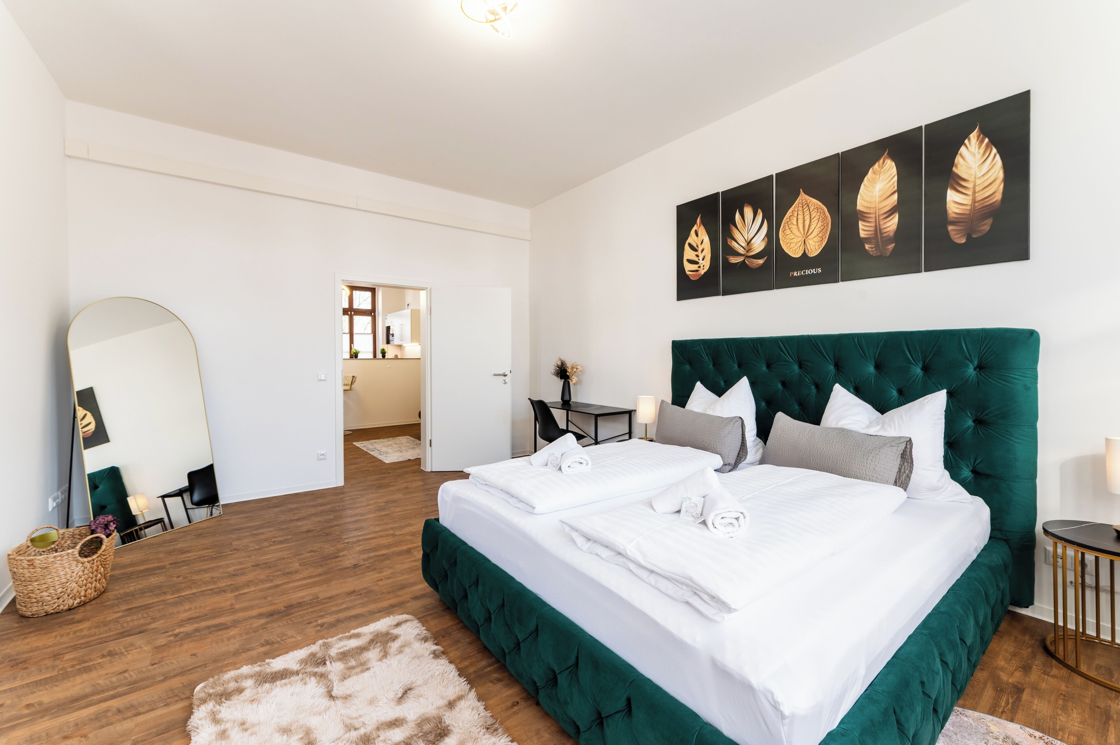 Ein Schlafzimmer mit einem großen Bett, einem Spiegel, Kunstwerken an der Wand und Blick in einen anderen Raum.