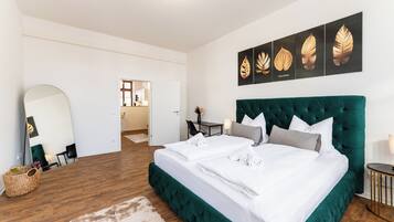 Ein Schlafzimmer mit einem großen Bett, einem Spiegel, Kunstwerken an der Wand und Blick in einen anderen Raum.