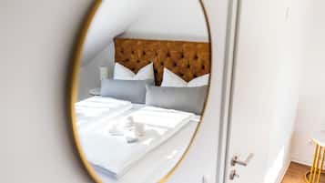 Een slaapkamer met een gestapeld hoofdbord, een bed met witte lakens en een ronde spiegel die de kamer weerkaatst.