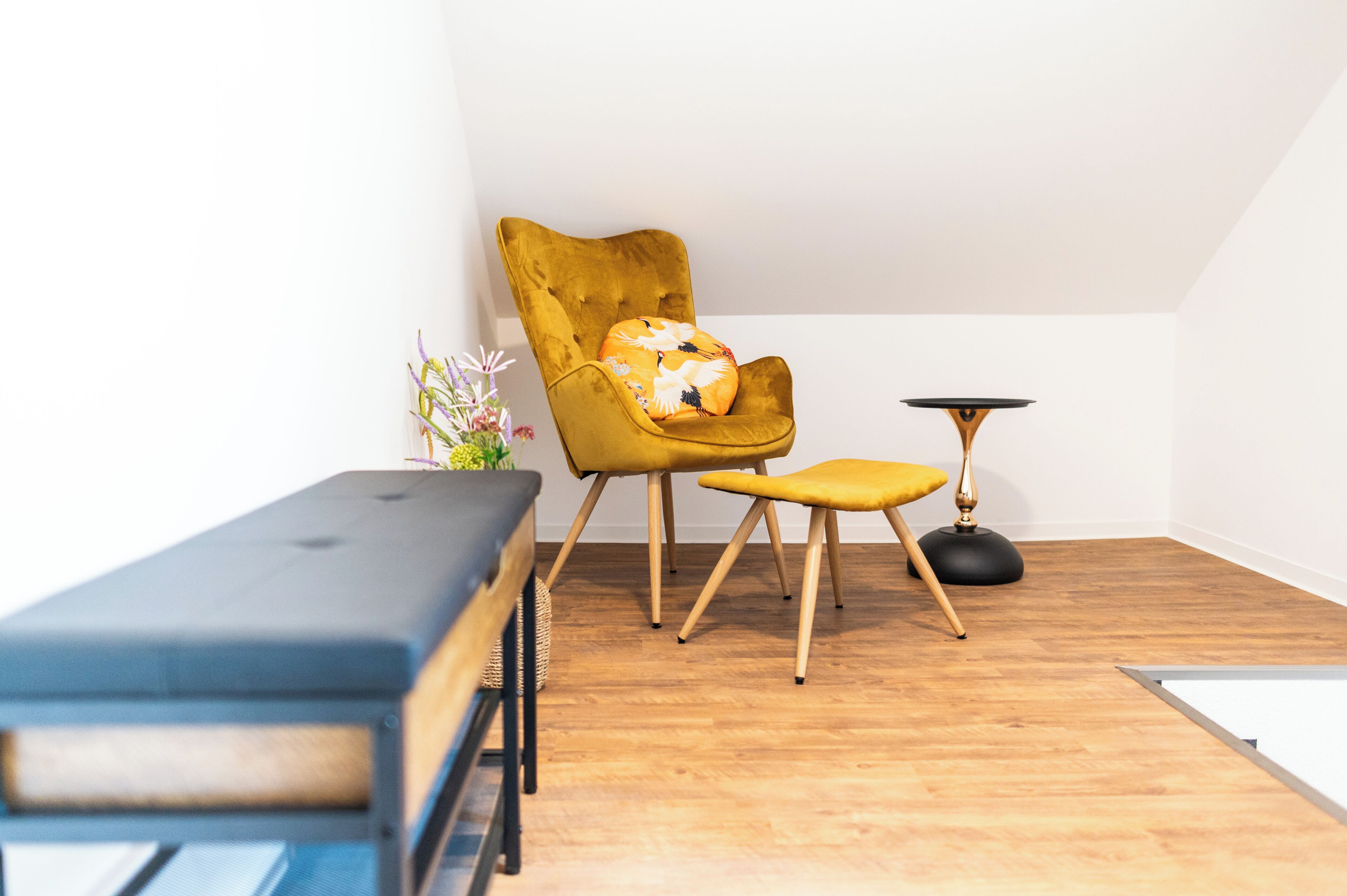 Une pièce comprenant un fauteuil jaune, un petit tabouret, une table ronde et un banc.