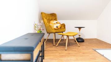 Une pièce comprenant un fauteuil jaune, un petit tabouret, une table ronde et un banc.