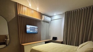 Une chambre d’hôtel avec un lit, un bureau, une télévision et une fenêtre avec des rideaux.