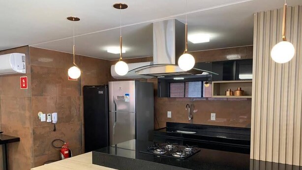 Une cuisine moderne dotée d’un îlot central, d’appareils électroménagers en acier inoxydable et de luminaires suspendus.