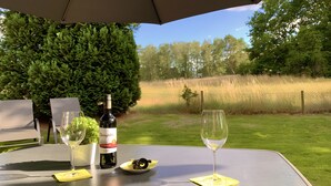 An outdoor table with a bottle of wine, two glasses, a plate with food, and a potted plant. - Nature-Inspired 100 m² Apartment with Fenced Garden, Terrace & Wi-Fi – Dog-Friendly (Neuzelle)