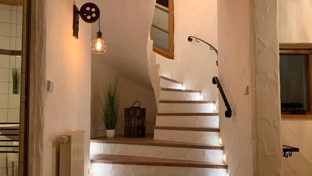 A staircase with a handrail, a wall-mounted light fixture, and a potted plant. - Nature-Inspired 100 m² Apartment with Fenced Garden, Terrace & Wi-Fi – Dog-Friendly (Neuzelle)