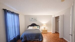 Une chambre à coucher comprenant un lit, une table de chevet, une œuvre d’art murale et une porte donnant sur une autre pièce.
