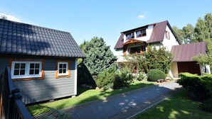 A residential area with two houses, one with a sloped roof and another with a flat roof, surrounded by greenery and a paved driveway. - Large Holiday Home With Private Garden (Choczewo)