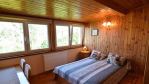 A wooden-paneled room with a bed, a table, and two windows. - Large Holiday Home With Private Garden (Choczewo)