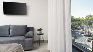 Een moderne woonkamer met een grijze bank, een bijzettafeltje met een plant en een wandgemonteerde televisie.