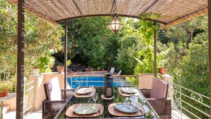 An outdoor dining area with a table set for four, surrounded by wicker chairs, under a pergola with a hanging lantern.