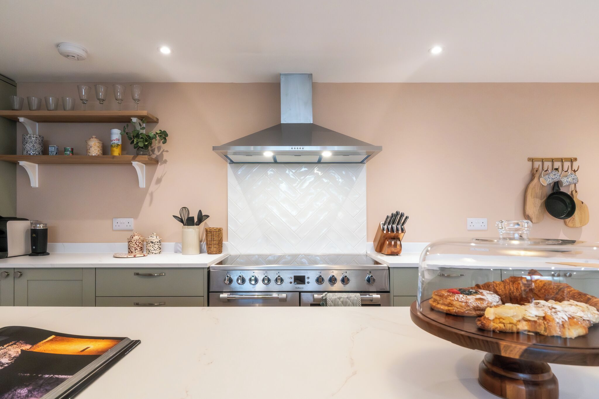 A kitchen with a stainless steel stove, a herringbone-patterned backsplash, and a glass display case with pastries.