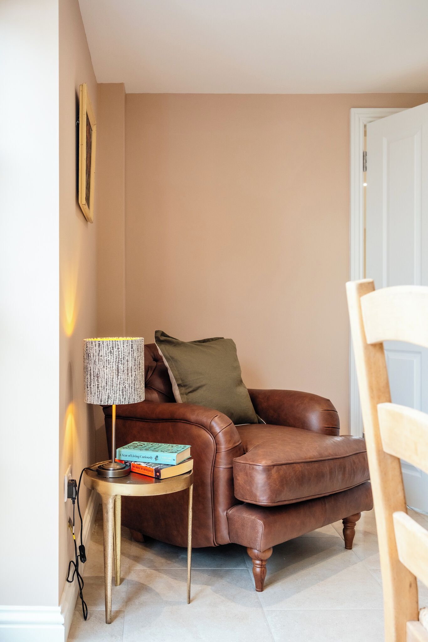 A brown leather sofa with a green pillow, a small round table with a lamp, and a few books.