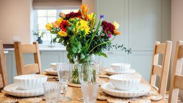 A dining table set with white plates, clear glassware, and a vase of colorful flowers.