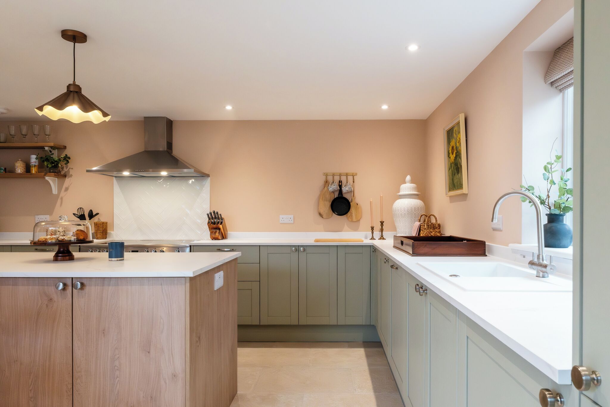 Une cuisine moderne dotée d’un îlot central, d’une hotte en acier inoxydable et d’un luminaire suspendu.