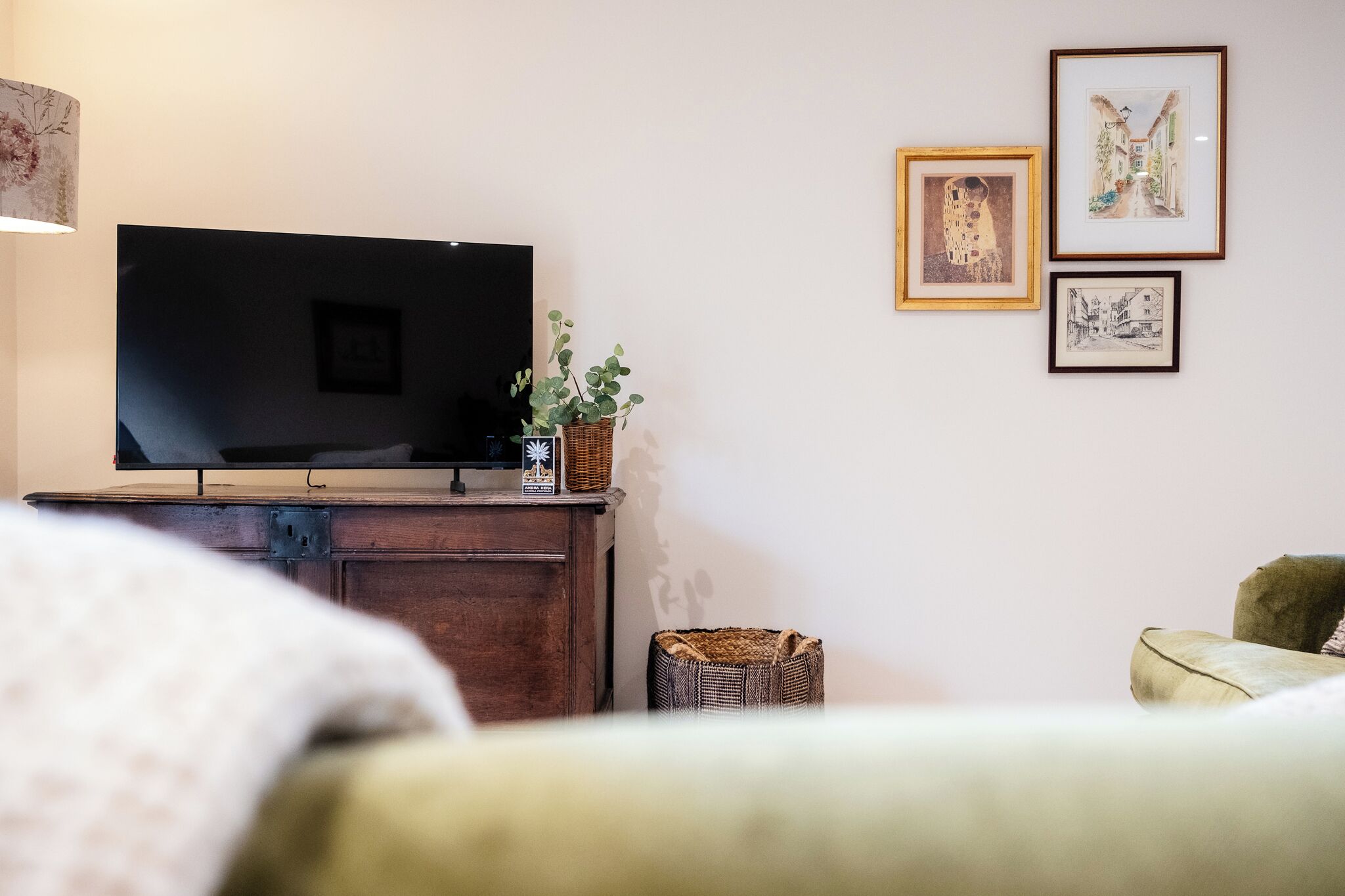 A room with a flat-screen TV on a wooden cabinet, a wicker basket, and framed artwork on the wall.