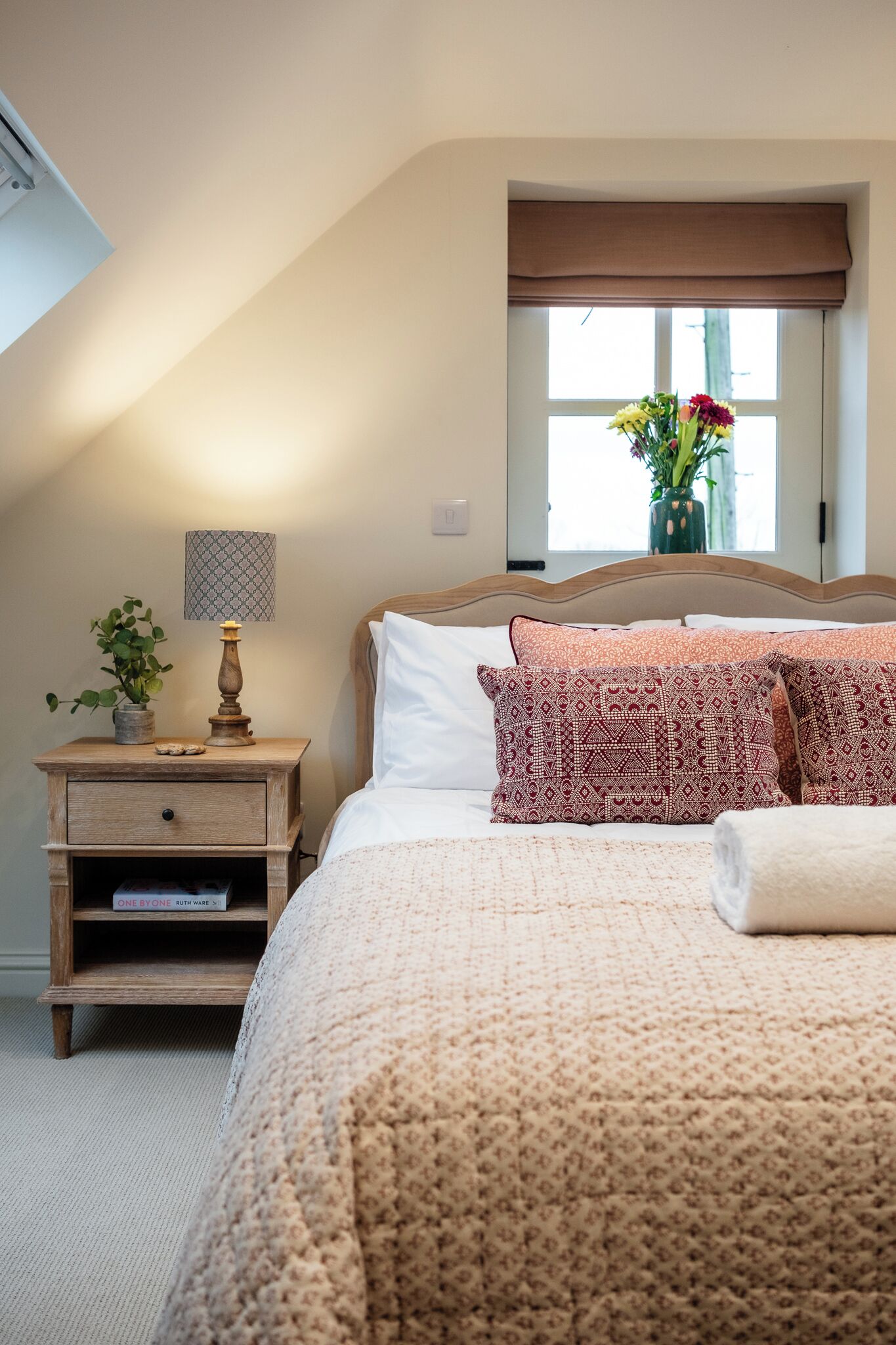 A bedroom with a bed, a nightstand, a lamp, a plant, and a window with a view.