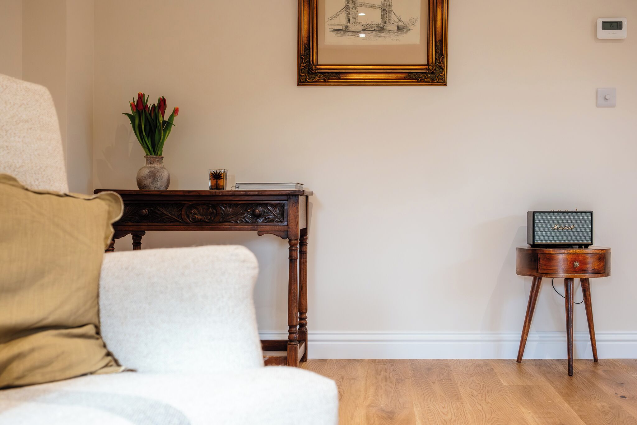Ein Zimmer mit einem weißen Sofa, einem Holznachttisch mit einer Vase roter Tulpen, einem gerahmten Bild an der Wand und einer kleinen Holzablage mit einem Lautsprecher.