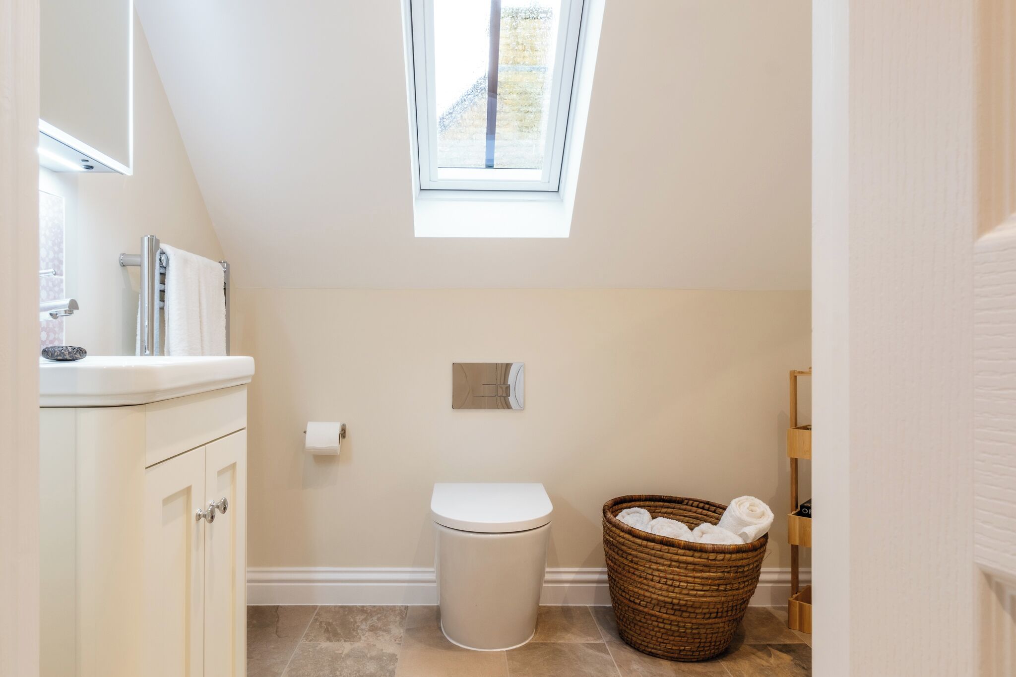 A small, modern bathroom with a skylight, a white toilet, a wicker basket, and a white sink.