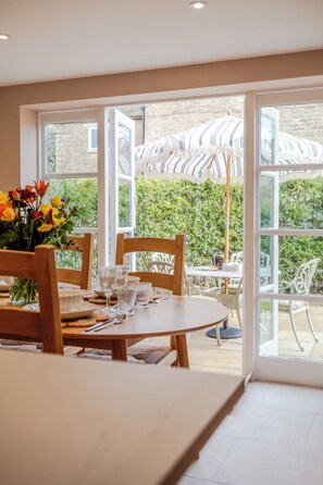 A dining area with a table set for four, chairs, and a vase of flowers. - The Stables Banham Cottages (Bourton-on-the-Water)