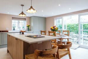 A modern kitchen with a central island, wooden chairs, and a dining table. - The Stables Banham Cottages (Bourton-on-the-Water)