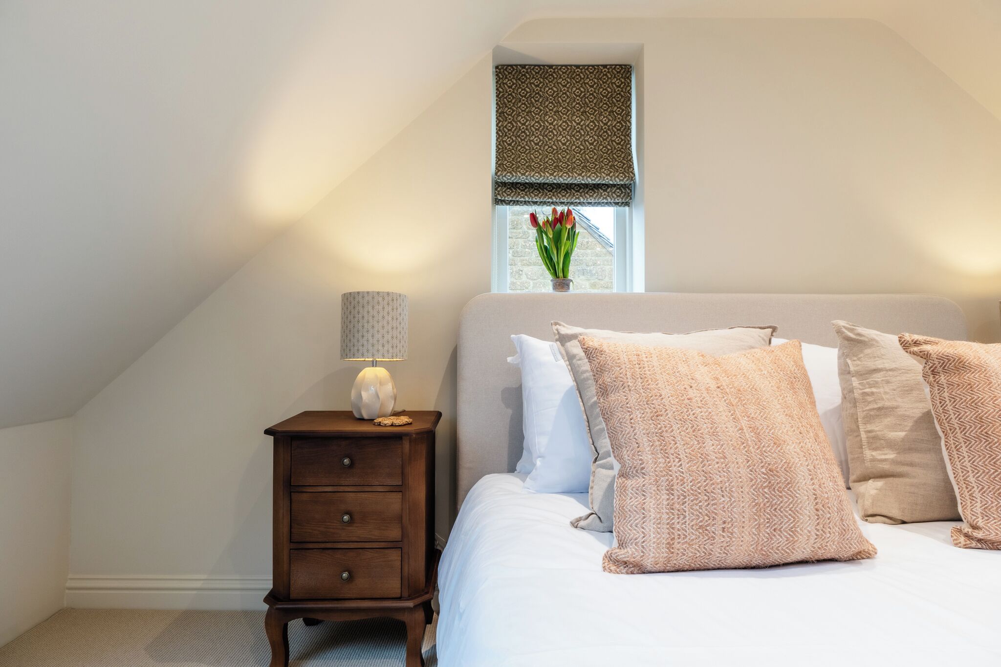 A bedroom with a bed, a nightstand with a lamp, a window with a view, and a small plant.