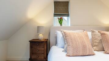 A bedroom with a bed, a nightstand with a lamp, a window with a view, and a small plant.