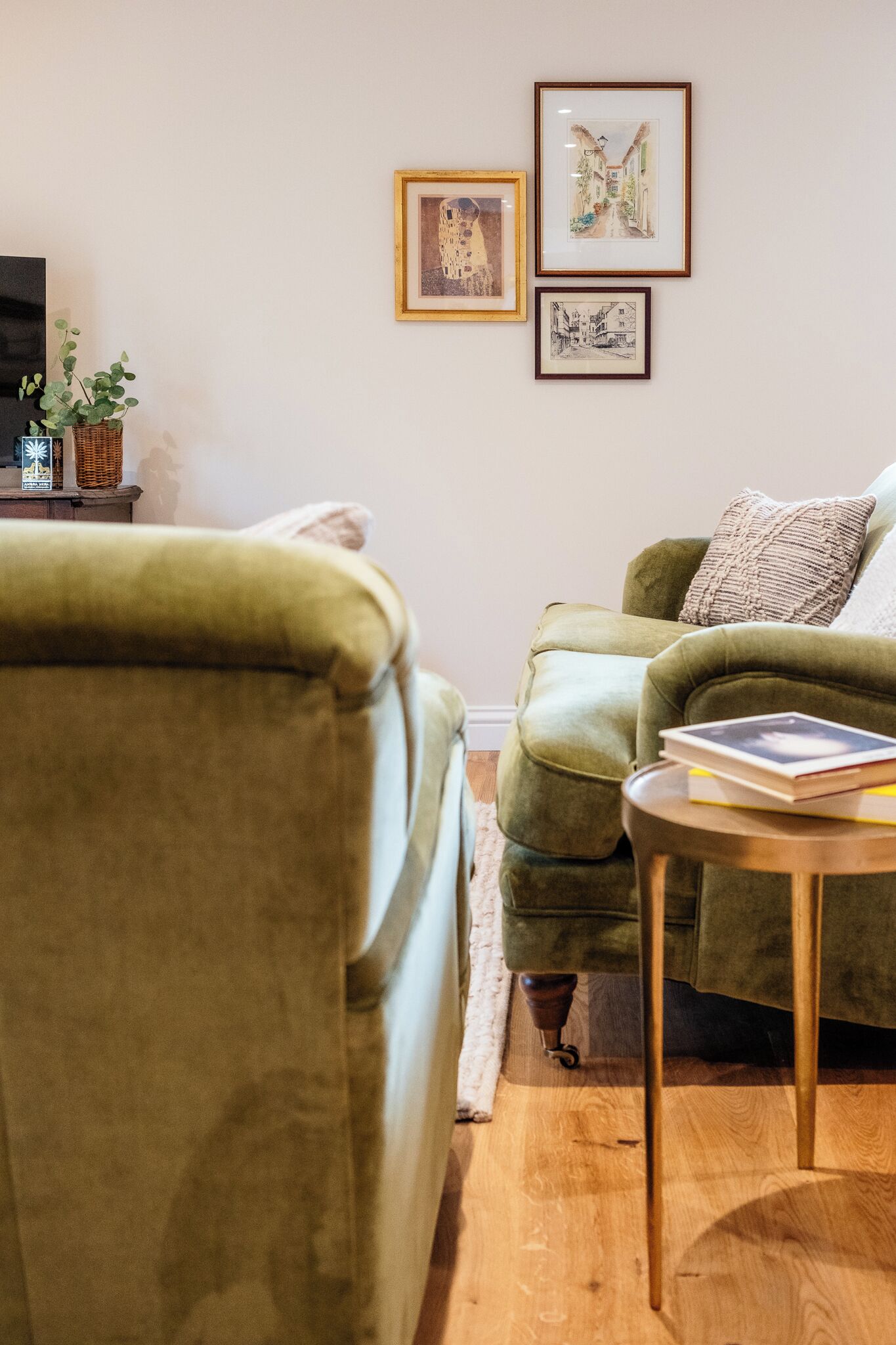 A living room with a green sofa, a small round table, and framed artwork on the wall.