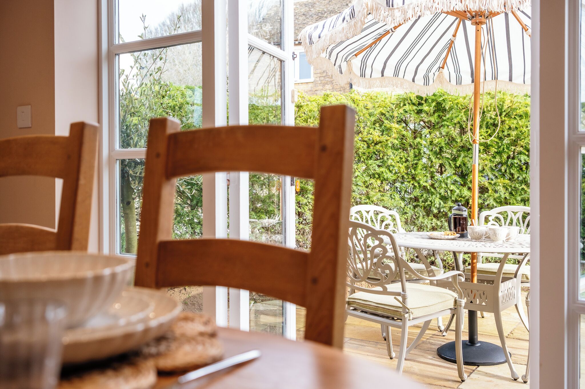 Un espace repas avec une table et des chaises, une vue sur la verdure et un grand parasol.