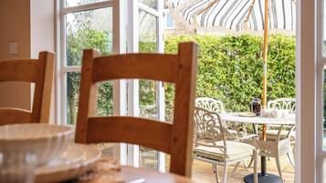 Un espace repas avec une table et des chaises, une vue sur la verdure et un grand parasol.
