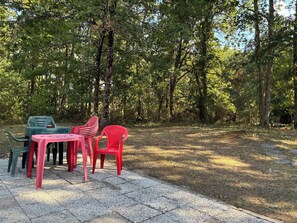 Un espace extérieur aménagé avec des chaises et des tables en plastique, entouré d’arbres.
