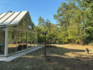 A greenhouse with a glass structure and a metal roof, surrounded by trees and a gravel path. - Private estate for 35 people • Lake Rillé (37) • Nature, Space, Community   (Rillé)