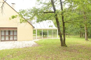 A building with a large glass conservatory, a paved driveway, and a grassy area with trees. - Large nature gîte 20 pers - Bar - Veranda - 1 ha - Lake Rillé (Rillé)
