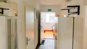 Un couloir étroit, avec des portes de chaque côté, un panneau indiquant la sortie, et un escalier menant à l’étage supérieur.