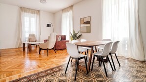 Een moderne woonkamer met een houten visgraatvloer, een eettafel met stoelen, een bank en een vloerlamp.