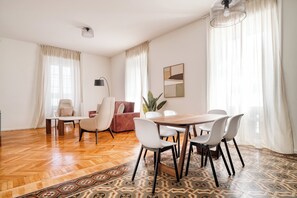 A modern living room with a wooden herringbone floor, a dining table with chairs, a sofa, and a floor lamp. - Elegant Flats near Guastalla Gardens (Milan)