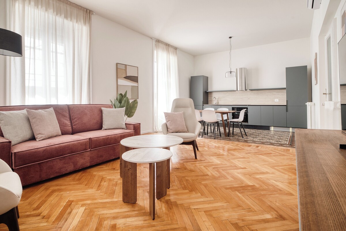 A modern living room with a sofa, two round tables, and a kitchen area in the background.