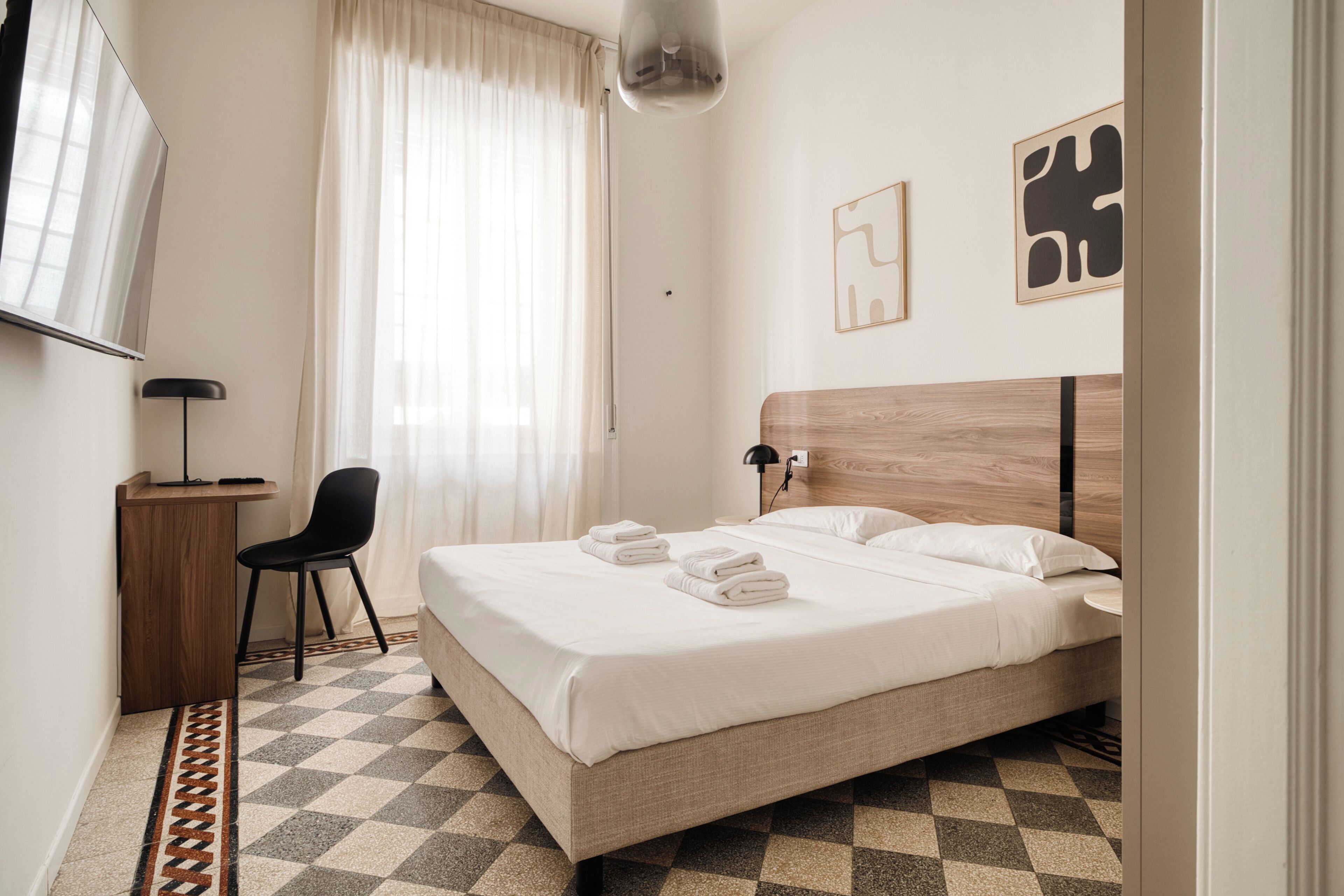A hotel room with a bed, a desk, a chair, and a window with curtains.
