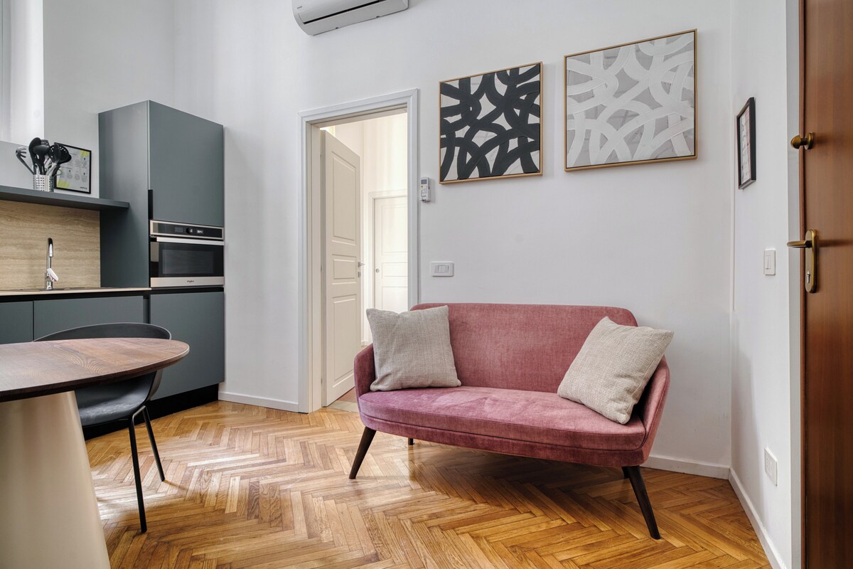 A modern kitchen with a herringbone floor, a pink sofa with cushions, and abstract wall art.