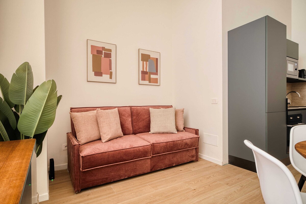 A modern living room with a red sofa, a dining table, and a kitchen area.