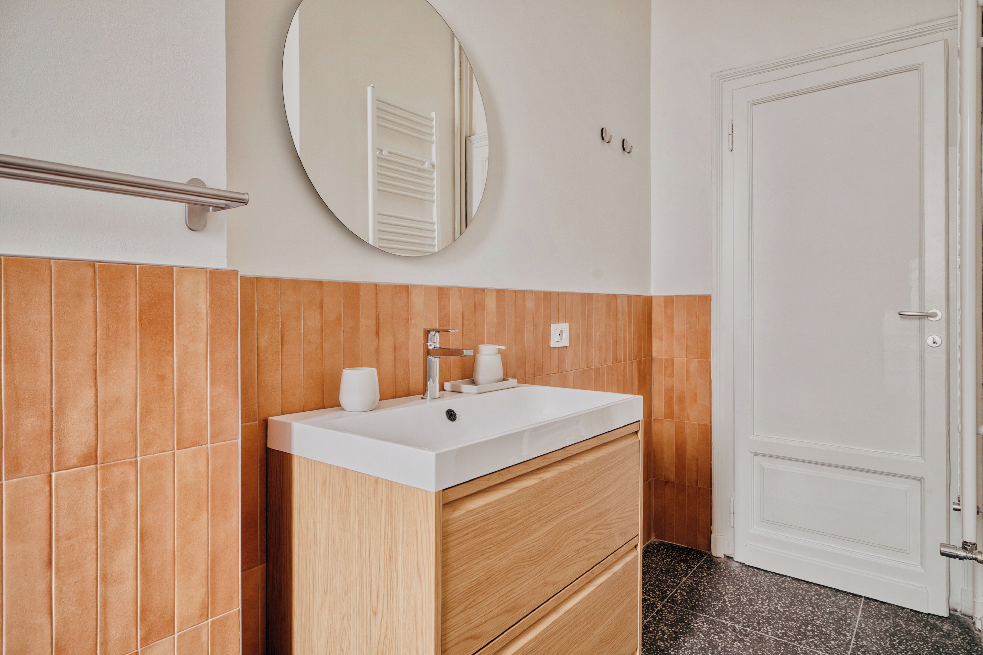 A bathroom with a white sink, wooden vanity, a round mirror, and a white door.