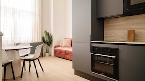 Een moderne keuken met een inbouwoven, een eethoek met tafel en stoelen, en een bank.