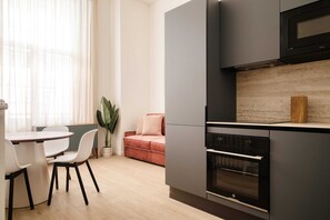 A modern kitchen with a built-in oven, a dining area with a table and chairs, and a sofa. - Elegant Flats near Guastalla Gardens (Milan)
