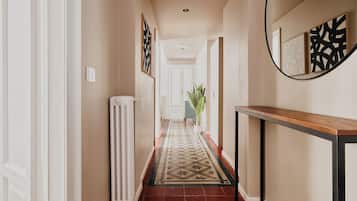 A hallway with a radiator, a patterned rug, a potted plant, and framed artwork on the walls.
