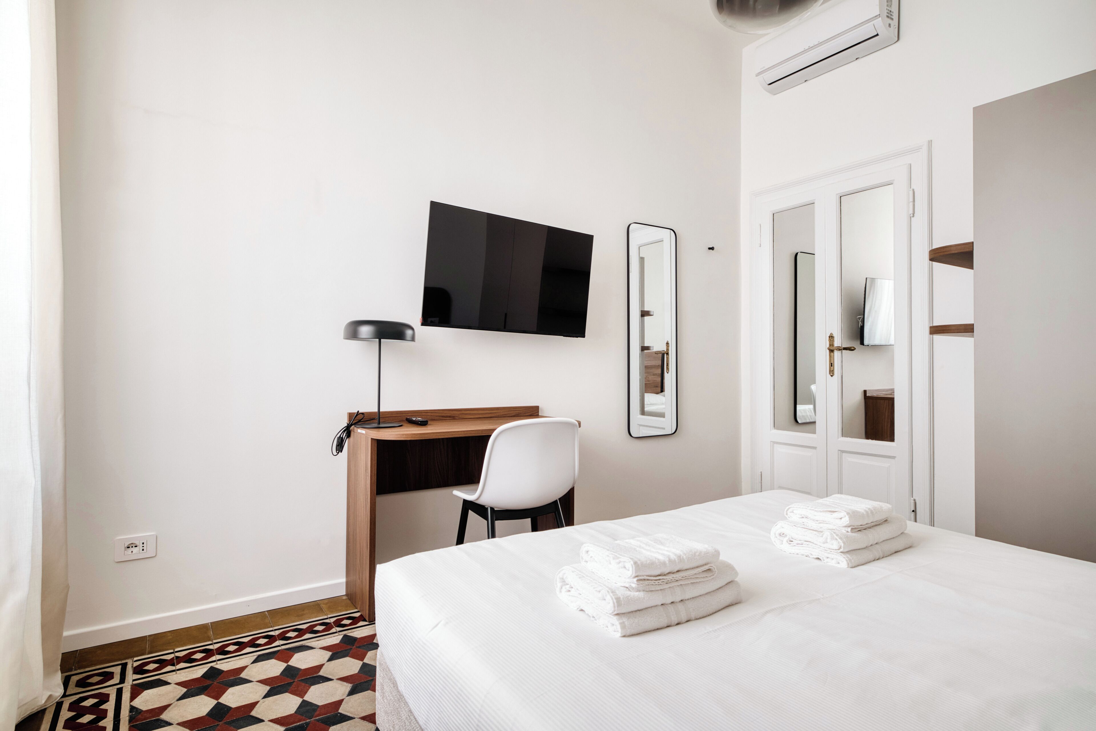 A hotel room with a bed, a desk, a chair, a TV, and a mirror.