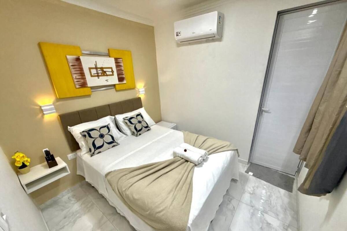 Une chambre à coucher bien rangée, avec un lit, des tables de chevet, un climatiseur fixé au mur et une porte.